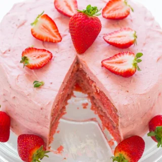 pink strawberry layer cake, missing a slice, with fresh strawberries on top