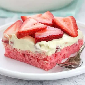 thin square of pink strawberry cake with white icing and fresh sliced strawberries on top, with fork on the side