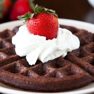 a chocolate brownie batter waffle on a white plate with cool whip and a fresh strawberry on top
