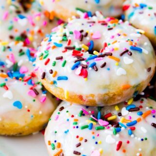 Plate full of funfetti donuts with white icing and rainbow sprinkles on top