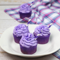 3 grape soda cupcakes on a white plate with another cupcake and a purple and white cloth in the background