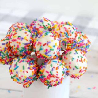 a bouquet of confetti cake pops with rainbow sprinkles in a cup