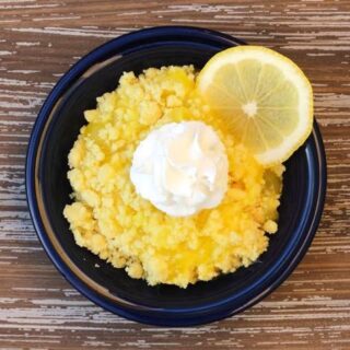 bowl of lemon dump cake with a fresh slice of lemon on the side and cool whip on top