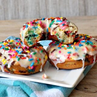 three funfetti donuts with white icing and rainbow sprinkles on top