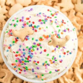 Bowl of funfetti dip with rainbow sprinkles on top, surrounded by animal crackers