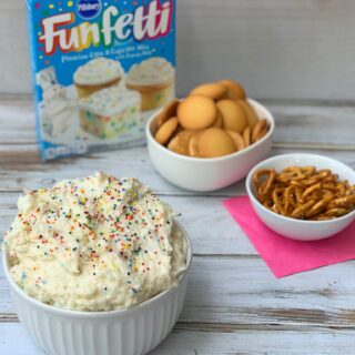 Bowl of funfetti dip with bowls of cookies for dipping in the background