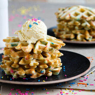Two plates with small stacks of funfetti waffles with cool whip and rainbow sprinkles on top