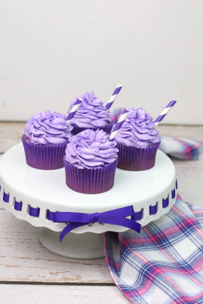 4 grape crush soda cupcakes on a white cake stand with a purple ribbon wrapped around it