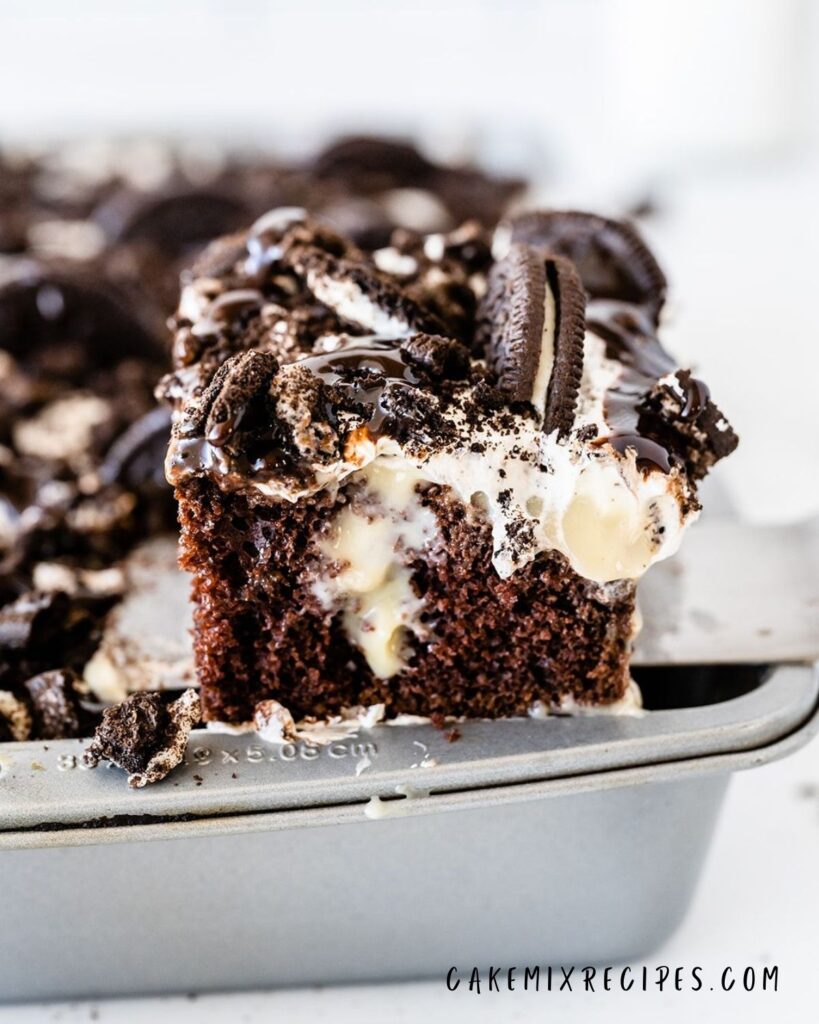 a spatula being used to lift out a piece of oreo poke cake from a pan filled with the rest of the jello poke cake