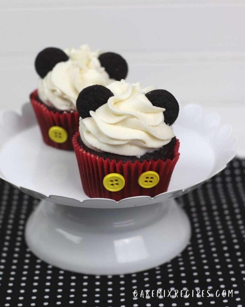 2 mickey cupcakes on a white cake stand on a black and white polka dot cloth