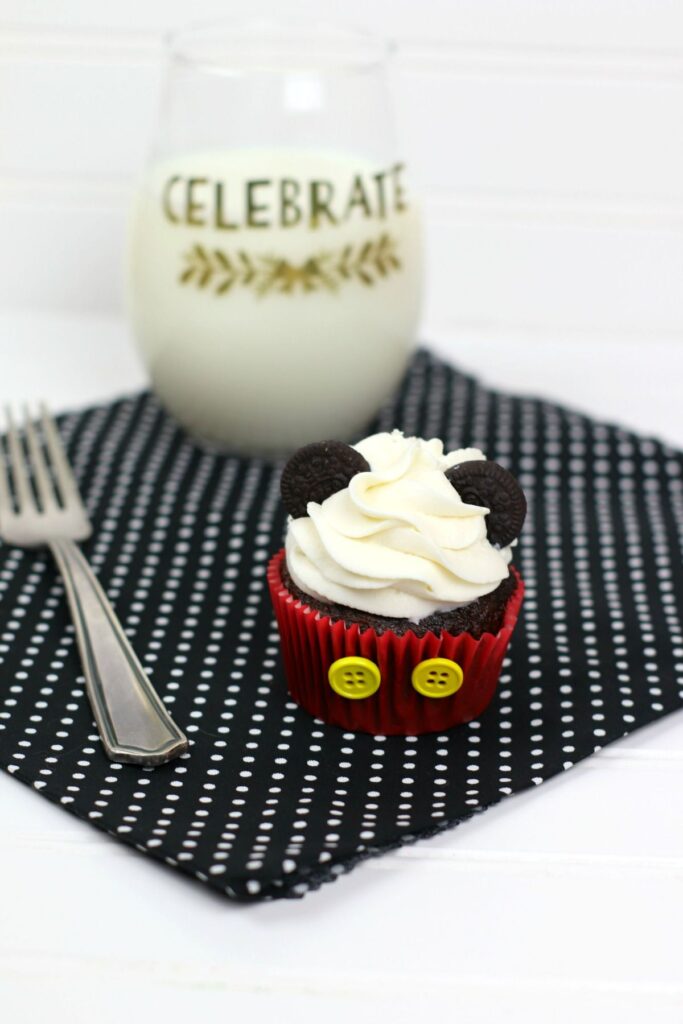 disney cupcake on a black and white polka dot cloth next to a fork and a glass of milk