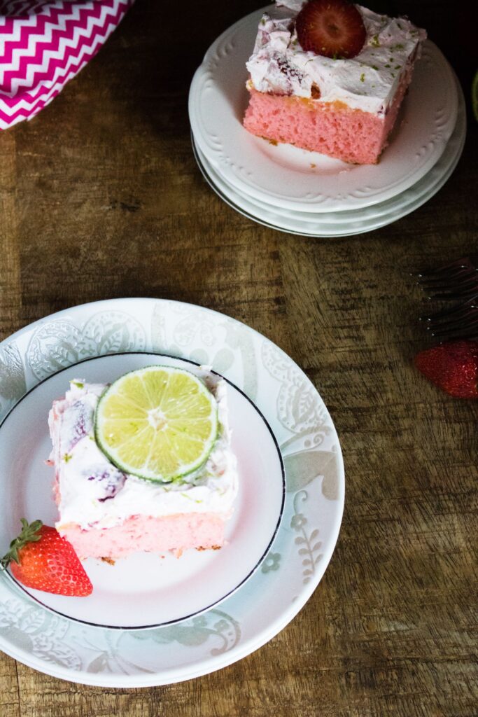 overhead view of a slice of strawberry margarita cake on two plates with another slice in the background