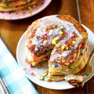 stack of golden brown funfetti pancakes with rainbow sprinkles and white frosting on top