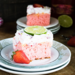 a slice of strawberry margarita cake on two plates with another slice in the background
