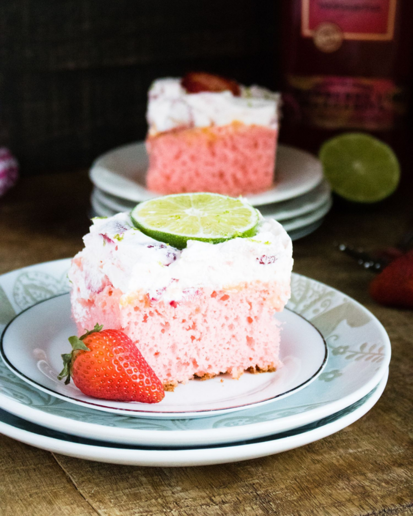 a slice of strawberry margarita cake on two plates with another slice in the background