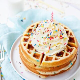 two stack of funfetti waffles with cool whip, rainbow sprinkles and a candle on top