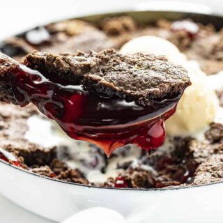 a glass dish of chocolate cherry dump cake with a spoon full taken out, oozing red sweet cherry filling