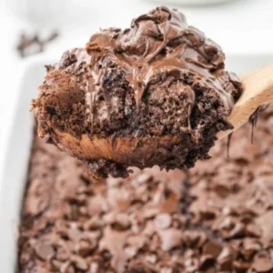 a piece of chocolate dump cake on a wooden spoon, with the rest in the background