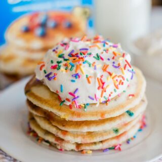 small stack of funfetti pancakes with white icing and rainbow sprinkles on top