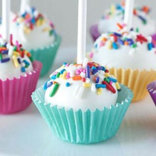 various upside down cake pops covered in white frosting and rainbow sprinkles, inside mini cupcake wrappers