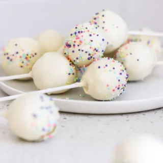 various white confetti cake pops with rainbow sprinkles on a white dish