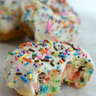 a funfetti donut with a bite taken out, with white icing and rainbow sprinkles on top