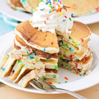small stack of funfetti pancakes with cool whip and rainbow sprinkles on top