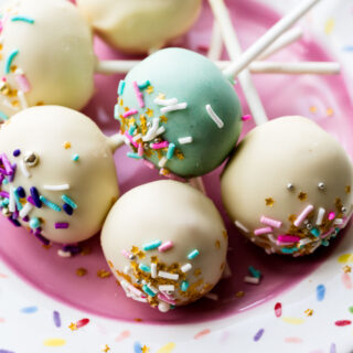 various confetti cake pops with rainbow sprinkles on top, on a pink and confetti printed plate