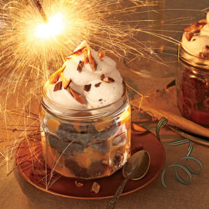 a small mason jar filled with banana brownie toffee pudding, topped with wiped cream, nuts and a festive sparkler