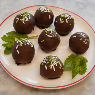 seven chocolate covered brownie mix truffles topped with white sprinkles, garnished with mint leaves on a white plate