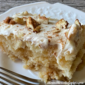 cinnamon roll poke cake with white frosting and nuts on top