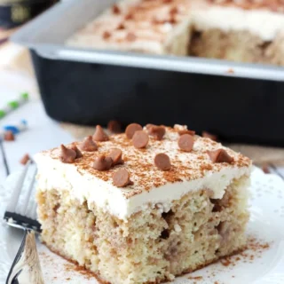 cinnamon roll poke cake with white frosting, chocolate chips and cinnamon sprinkled on top