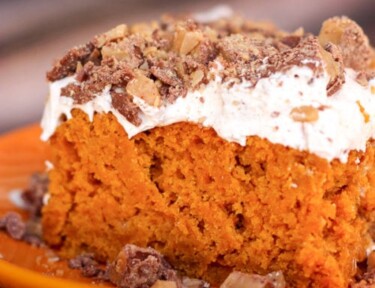 pumpkin poke cake with frosting and sprinkled nuts on top