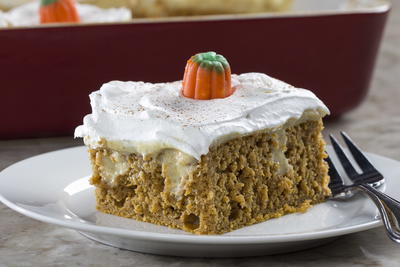 pumpkin spice poke cake with white frosting and a pumpkin candy corn on top