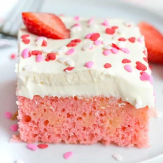 pink strawberry poke cake with vanilla pudding, a fresh strawberry and sprinkles on top
