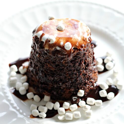 Hot Chocolate Mug Cake on a white plate with fudge drizzle and miniature marshmallows on top