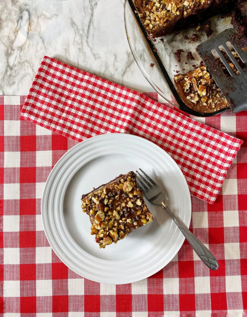 overhead view of a slice of caramel chocolate Poke Cake topped with nuts on a plate with a fork on the side.