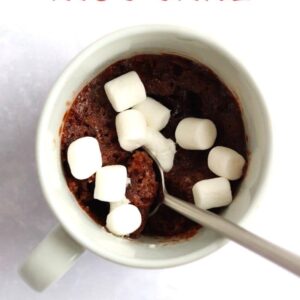 hot cocoa mug cake in a white mug with mini marshmallows on top, and a spoon inside
