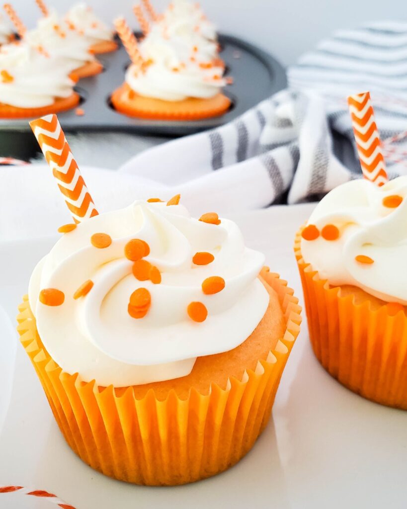 a closeup of 2 creamsicle orange cupcakes with more cupcakes in a pan in the background