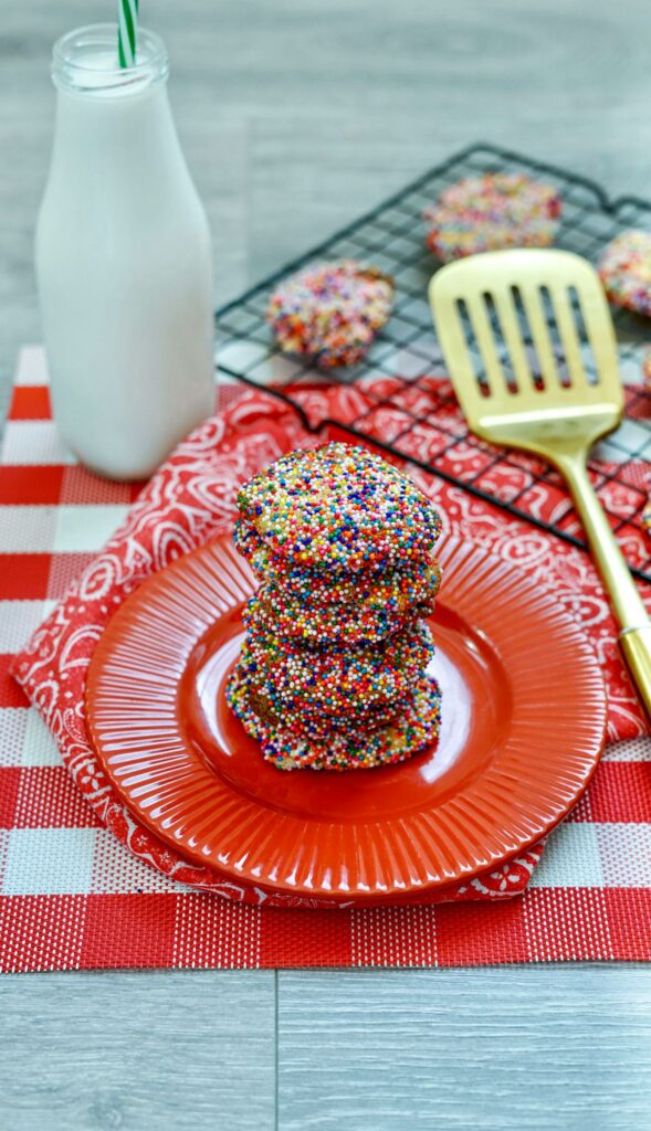 Sprinkle Cookies in the Air Fryer on a plate and cooking rack with red placemat in the background next to a bottle of milk and golden spatula.