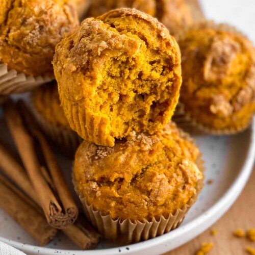 moist golden brown pumpkin muffins with some cinnamon sticks on the side