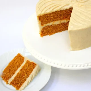 pumpkin spice cake covered in white frosting with a slice taken out on a plate