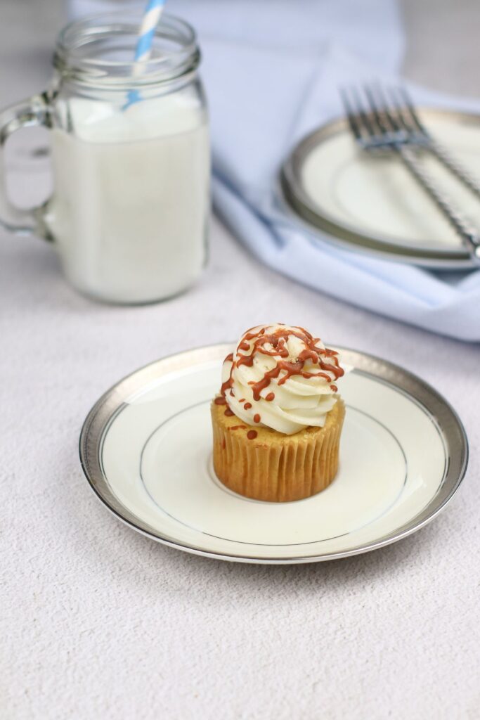 Cinnamon Cupcake on a plate with a glass of milk and 2 forks on a plate in the background.