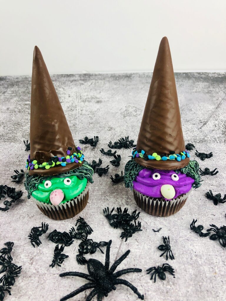 two Witch Cupcakes one green and one purple with plastic spiders in the background