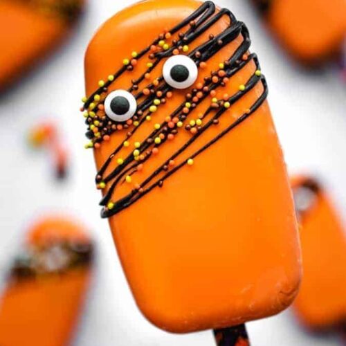 Spooky orange cakesicle with candy eyes and chocolate drizzle