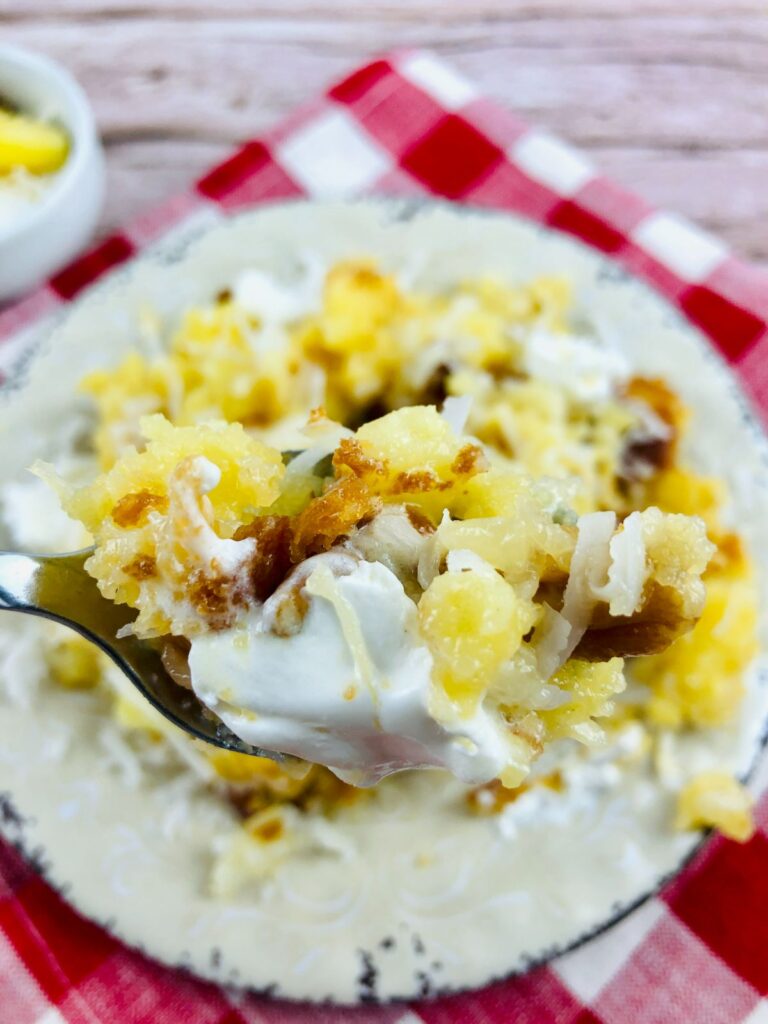 spoonful of cake with pineapple and coconut above more cake on a plate. 