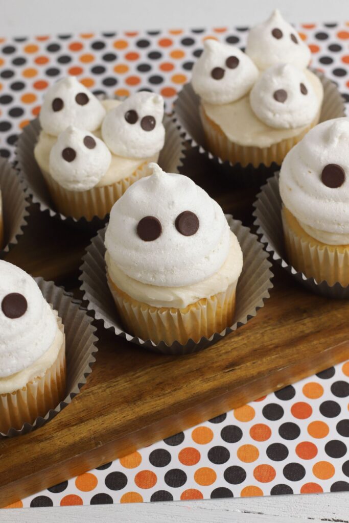 ghost cupcakes on a brown board on an orange and black polka dot cloth.