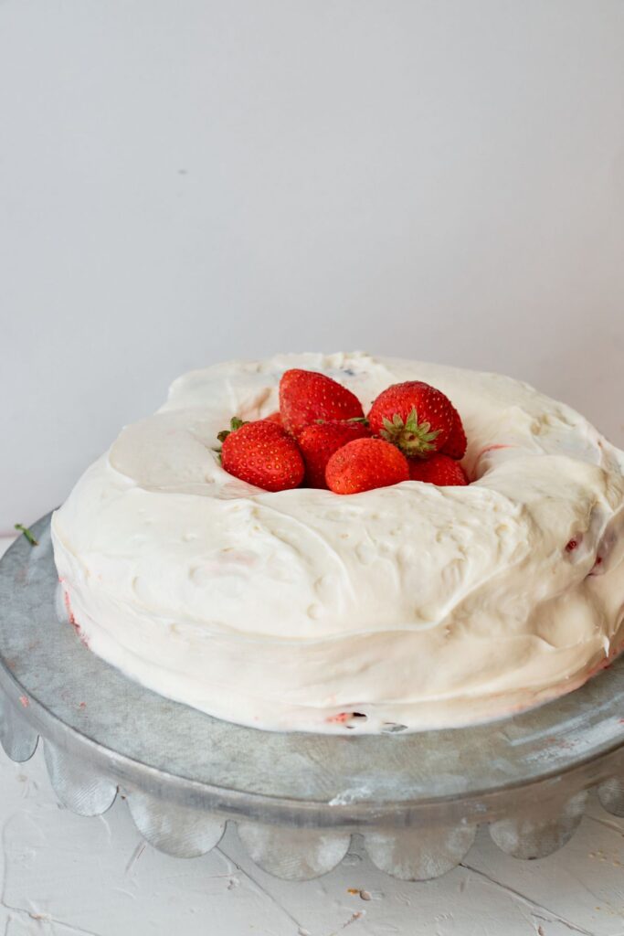 Vanilla strawberry cake on a cake stand with a handful of strawberries on top.