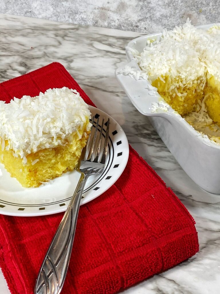 A slice of Pineapple Coconut Poke Cake on a small plate with a fork on the side.