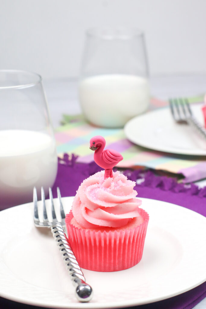 a strawberry cupcake on a plate with a glass of milk and fork on the side.
